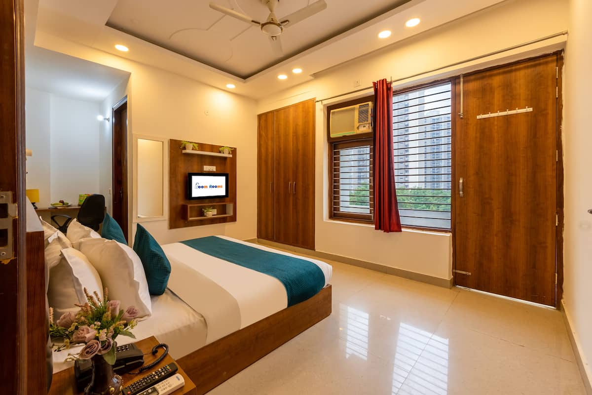 Un dormitorio con cama, mesita de noche, televisor, armario y ventana con cortinas.
