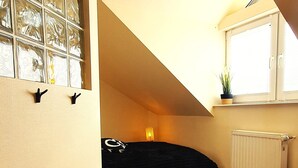 A room with a sloped ceiling, a round woven rug, a bench, a potted plant, and a window with a radiator. - Happy Ocean - ground floor apartment: vacation with family & dog, 2 min. to the beach. (Pobierowo)