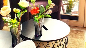 A cozy seating area with a cushioned chair, a round table, and two vases with flowers. - Happy Ocean - ground floor apartment: vacation with family & dog, 2 min. to the beach. (Pobierowo)