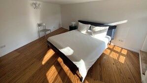 A bedroom with a large bed, a chair, a nightstand, and a wall-mounted light fixture.