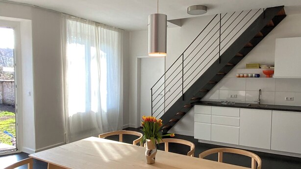 A modern kitchen with white cabinets, a black staircase, and a wooden dining table with chairs.