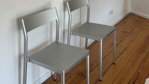 Two modern chairs with metal frames and grey seats, positioned against a white wall with a wall-mounted light fixture.