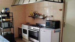 A kitchen with a gas stove, oven, microwave, and a shelf with kitchen items. - Gite la Rose des Alpes (Serres)
