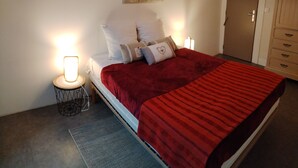 A neatly made bed with a red blanket, two bedside lamps, a wall art piece, and a wooden wardrobe. - Gite la Rose des Alpes (Serres)
