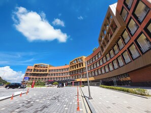 Un bâtiment moderne à la façade incurvée, doté de nombreux balcons, se dressant sous un ciel d’un bleu limpide.