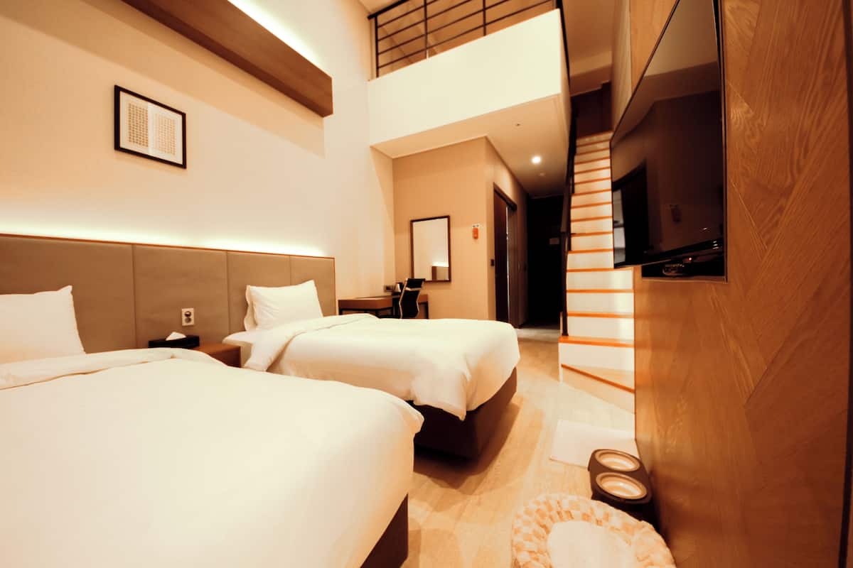 A hotel room with two beds, a TV, and a staircase leading to an upper level.
