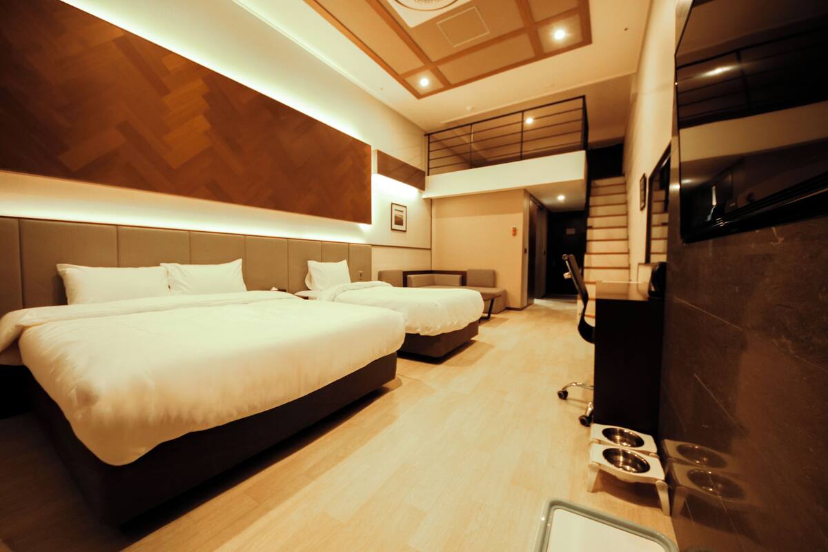 A hotel room with two beds, a wooden wall, a ceiling light, a staircase, and a TV.