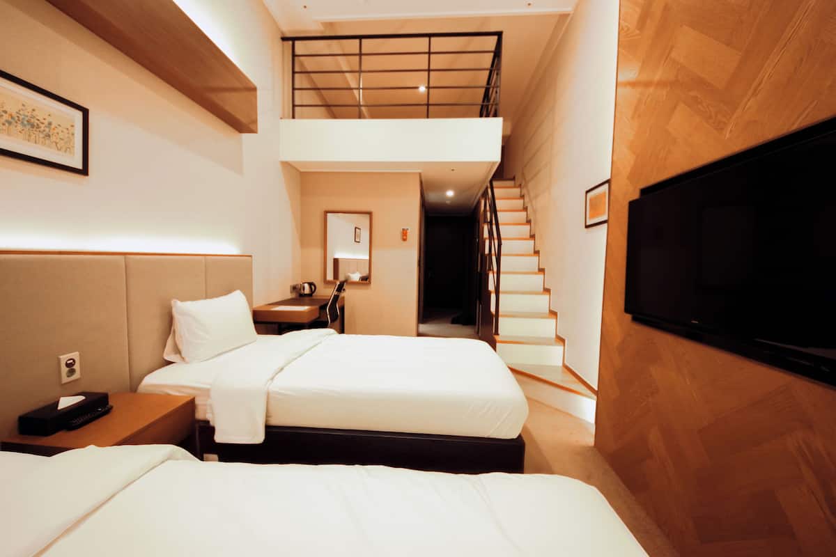 A hotel room with two beds, a TV, a desk, and a staircase leading to an upper level.