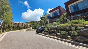 Un edificio moderno con techo plano y amplios ventanales, rodeado de follaje y rocas.
