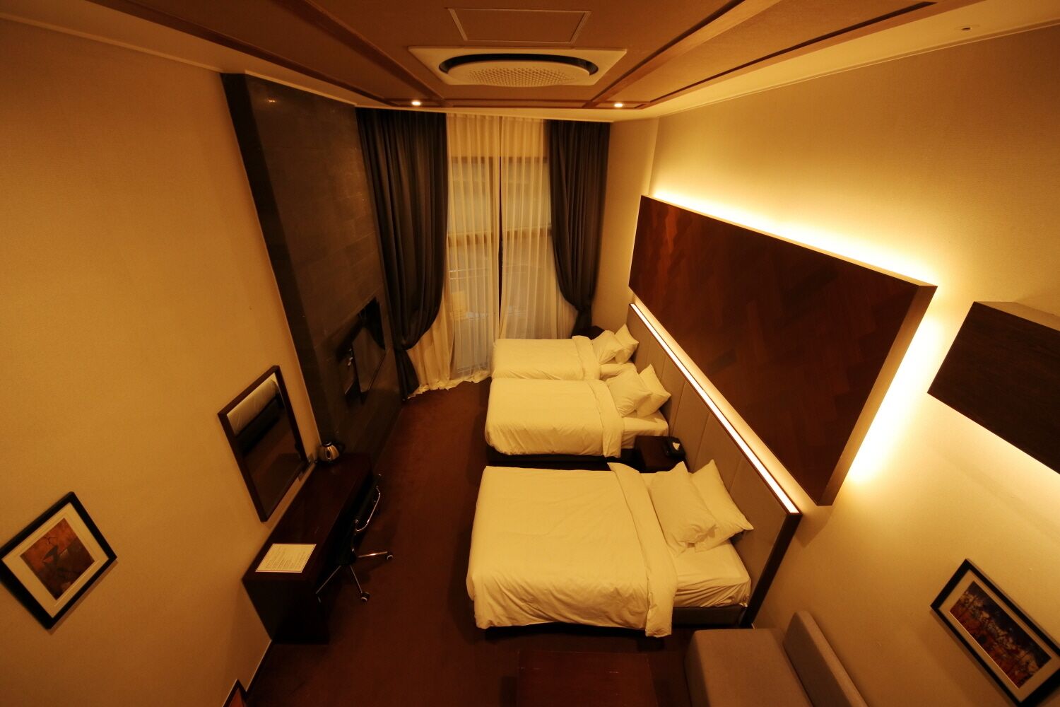 Een hotelkamer met twee enkele bedden, een bureau met stoel, een grote spiegel en een televisie.