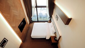 Habitación de hotel con cama, mesita de noche, ventana con cortinas y vista a un área de estar al aire libre.