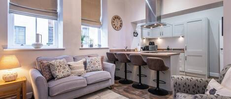 A modern living room with a sofa, a coffee table, a rug, and a bar area with stools.