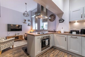 A modern kitchen with a built-in oven, a large island with a sink, and a flat-screen TV mounted on the wall.