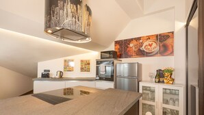 Cocina moderna con una isla central, horno empotrado, microondas y refrigerador. Hay armarios de pared y una obra de arte con temática de café sobre el mostrador.