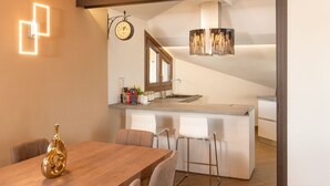 Una cocina moderna con una isla central, una zona de comedor con mesa y sillas de madera, y un reloj visible en la pared.