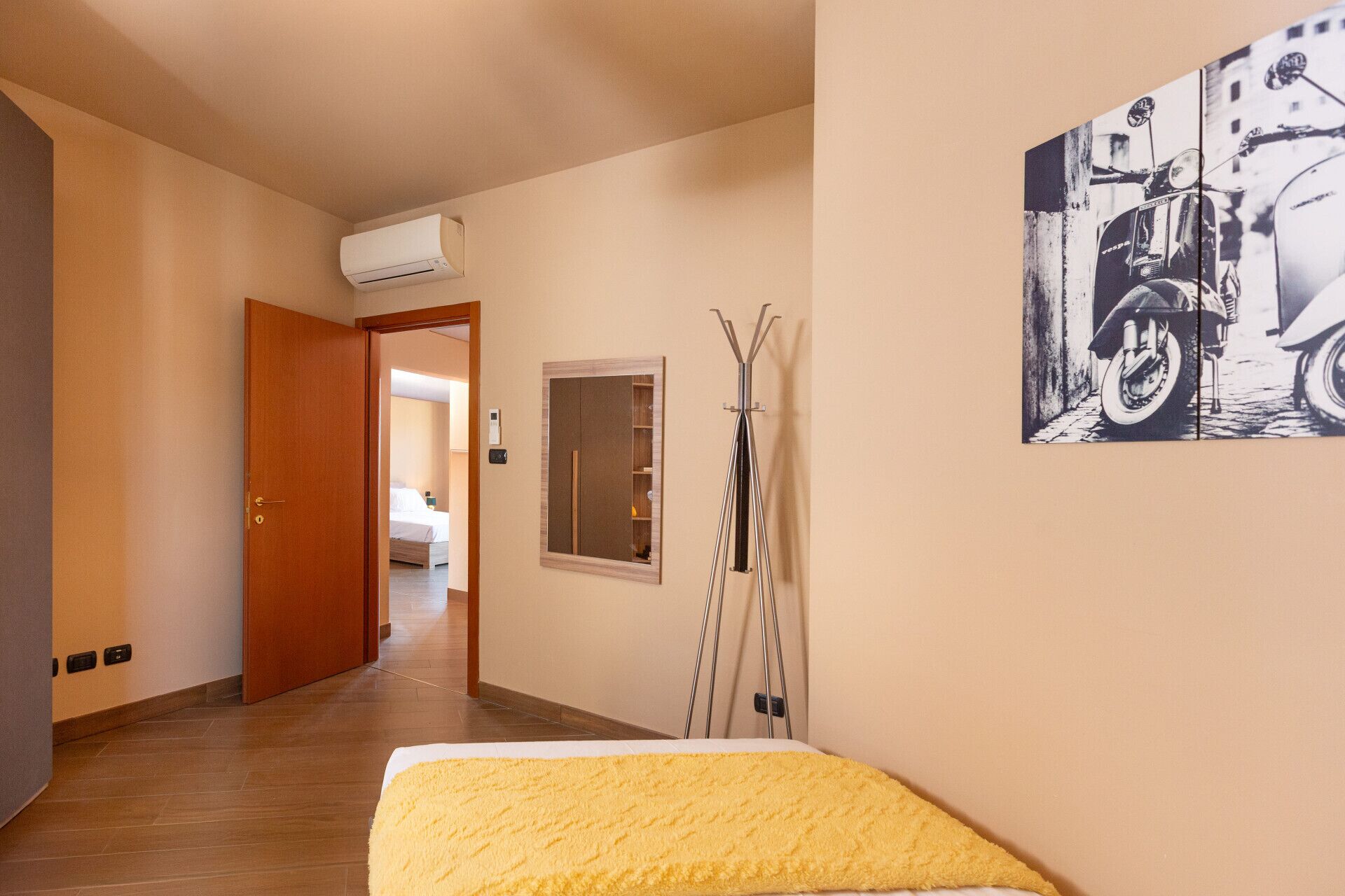 Une chambre d’hôtel comprenant un lit, un miroir, un climatiseur, un porte-manteau et un tableau accroché au mur.