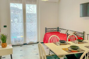 Quarto compacto com cama, mesa de jantar posta para dois e uma janela grande com vidro fosco.