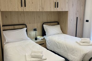 Une chambre d’hôtel avec deux lits simples, des têtes de lit en bois, une table de chevet avec une lampe et une petite table avec un livre.