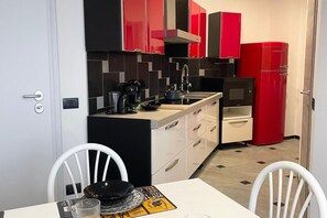 A compact kitchen with red and black cabinets, a microwave, and a red refrigerator. - Bnbook Residenza Balzarotti 1 (RHO)