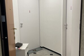 Ein schmaler, geschlossener Aufzug mit einem kleinen Schalter und einer Fußmatte auf dem Boden.