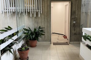 Um corredor com plantas em vasos, piso de azulejos e uma porta que dá para outro quarto.