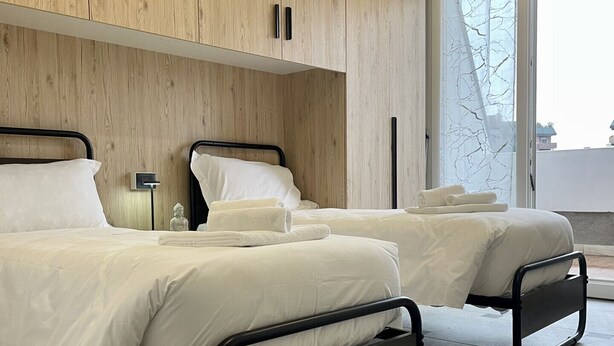 A modern bedroom with two beds, wooden paneling, and a large window. - Bnbook Residenza Balzarotti 1 (RHO)