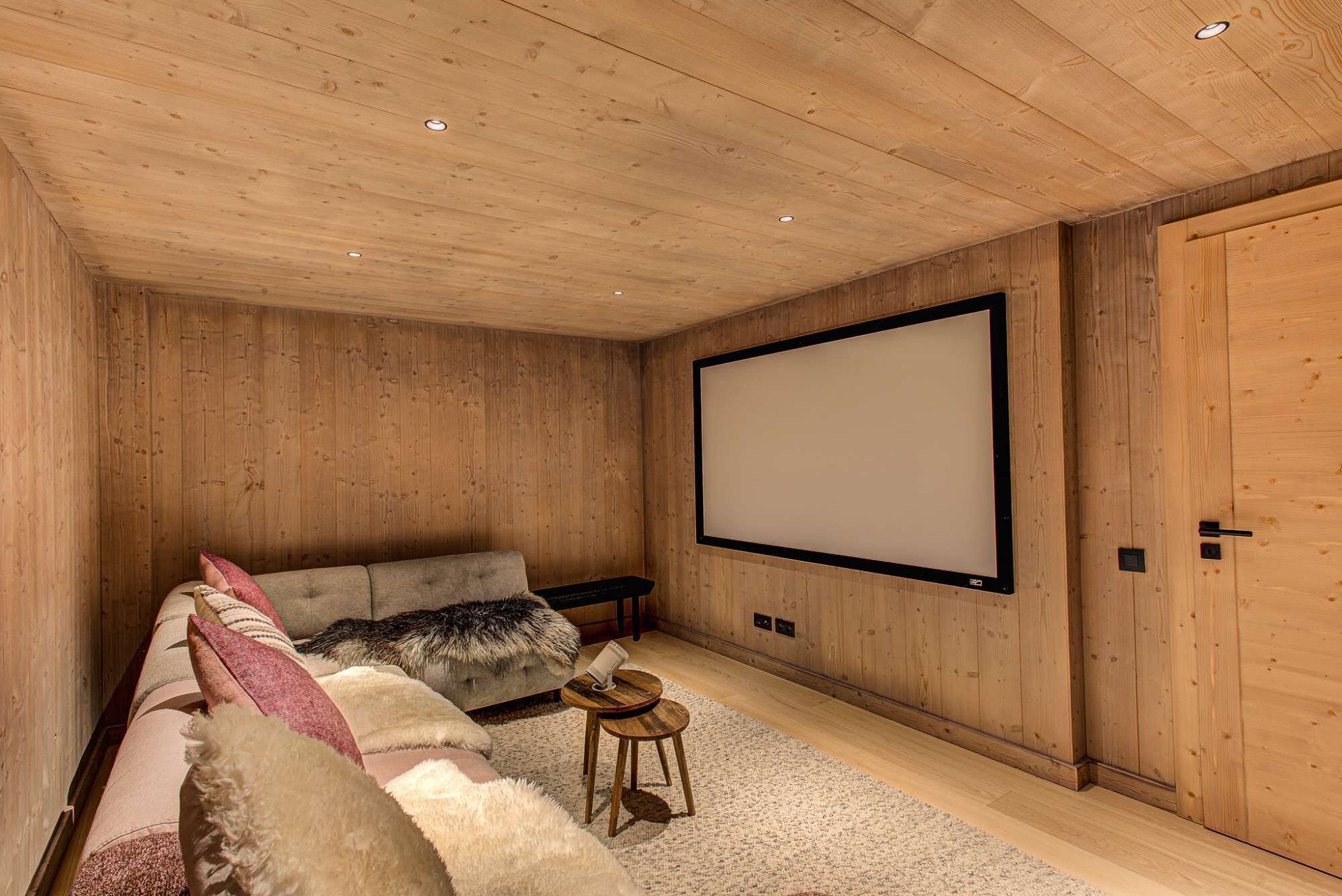A cozy room with a wooden ceiling, a large screen, a sofa, and a small table.