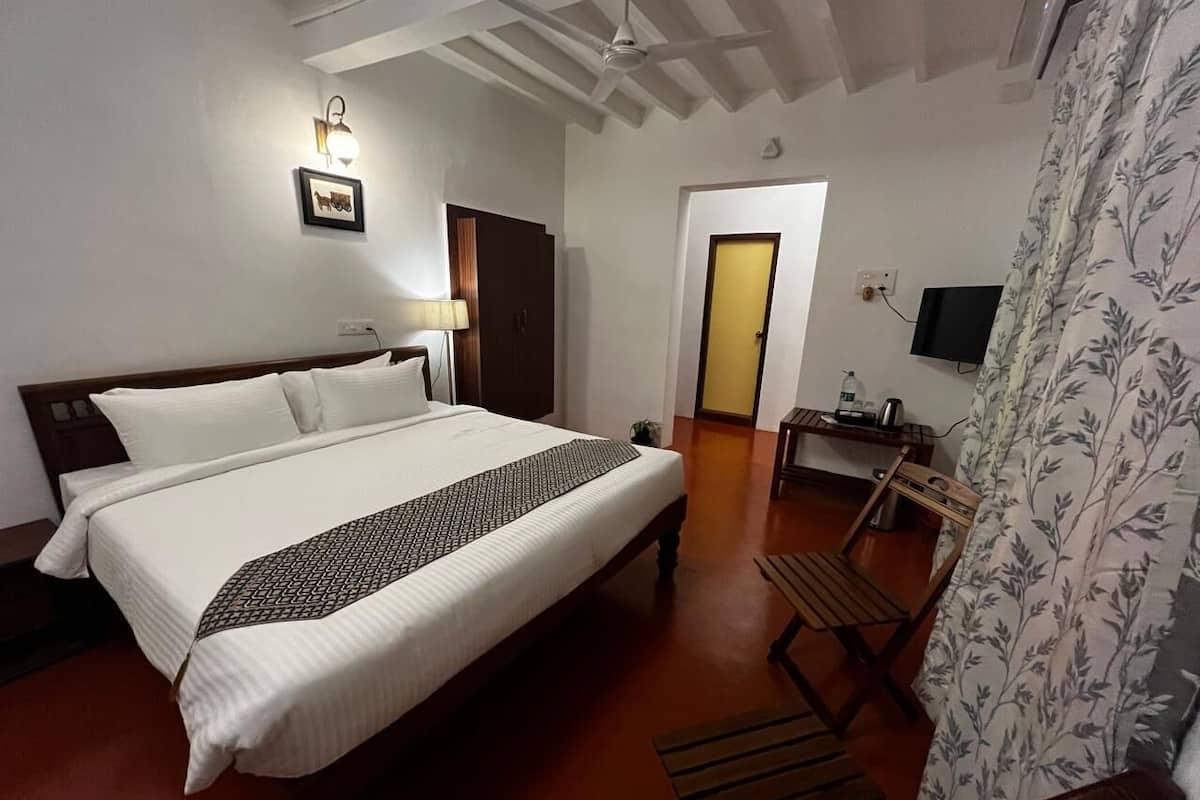 A bedroom with a bed, a desk, a chair, a TV, and a door.