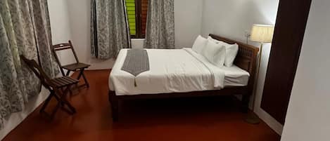A bedroom with a bed, a chair, a desk, a ceiling fan, and a window with curtains.