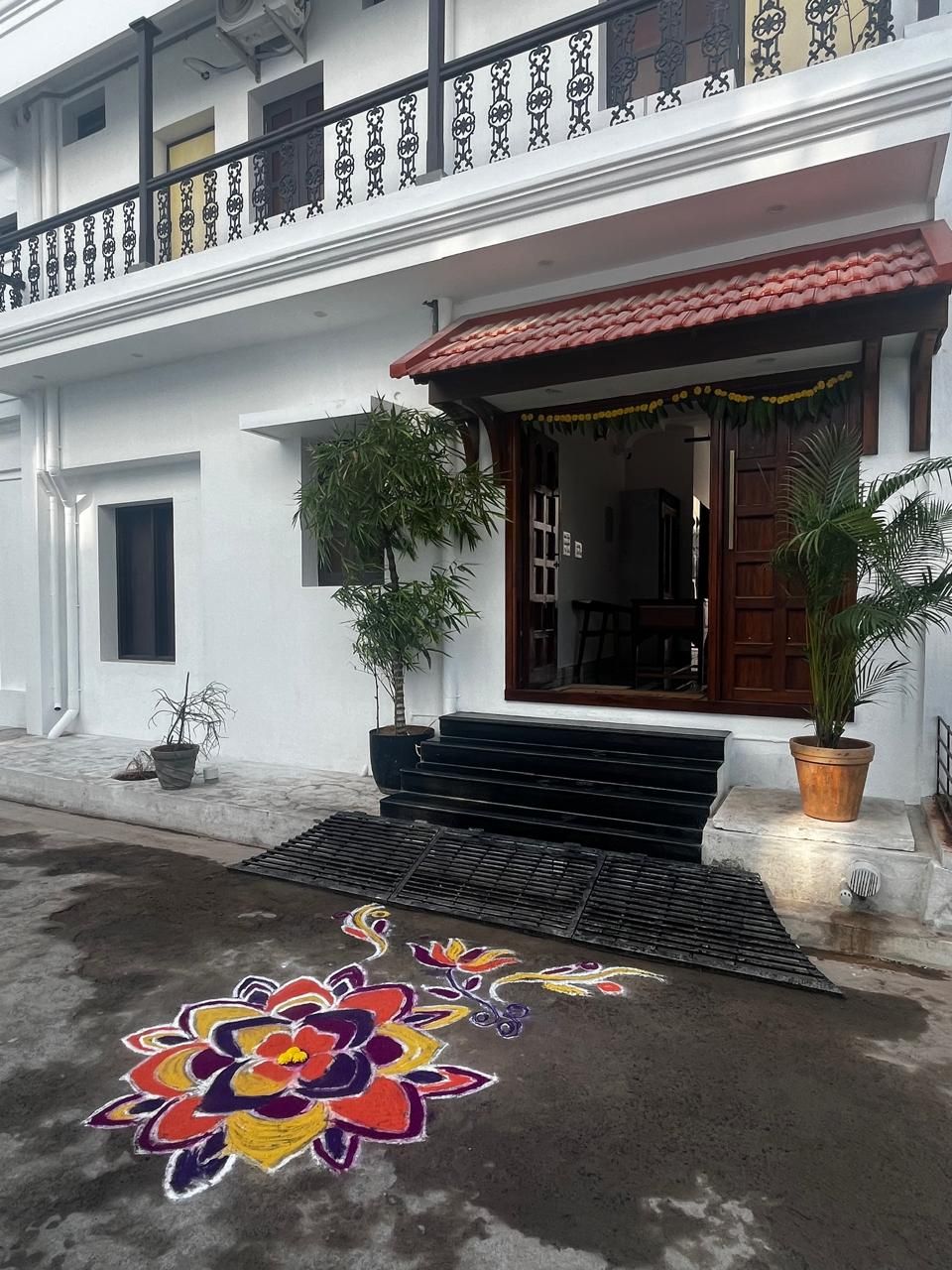 A two-story building with a balcony, a red-tiled roof, and a colorful floral ground decoration.