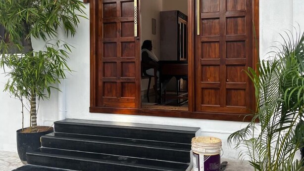 A traditional wooden house with a tiled roof, a wooden door, and a staircase leading to the entrance. - Villa Vedapuri (Puducherry)