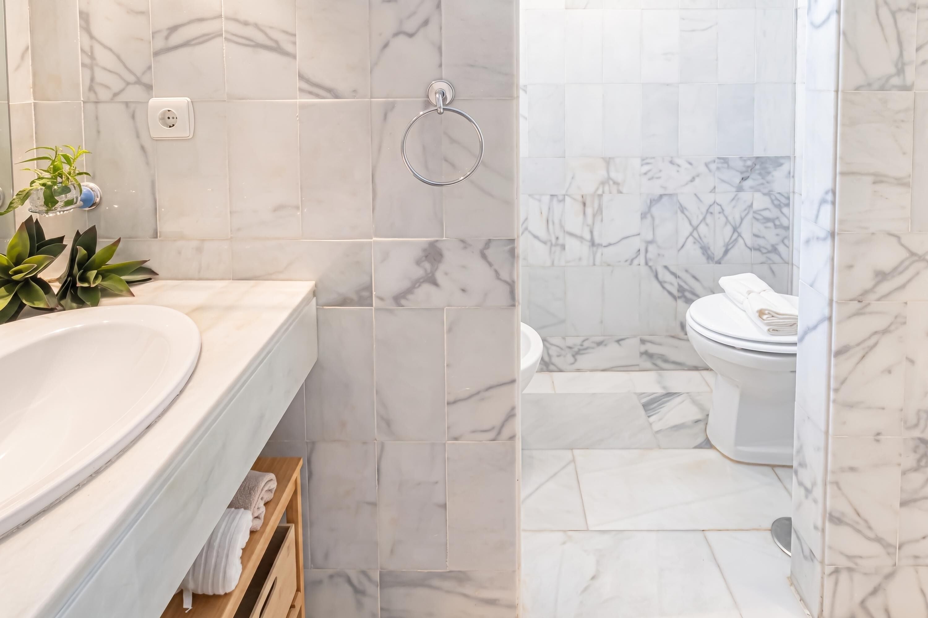 Un baño con lavamanos de mármol, inodoro y zona de ducha.