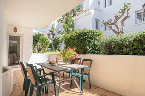 An outdoor patio with a table and chairs, a potted plant, and a white wall.
