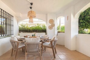 A patio with a round table, wicker chairs, and a hanging light fixture.