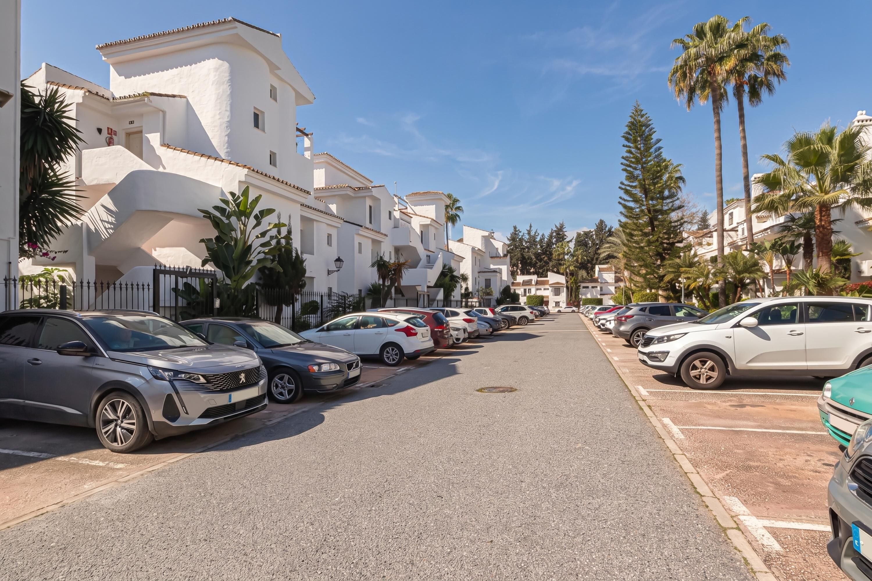 A street lined with parked cars and white buildings with balconies.