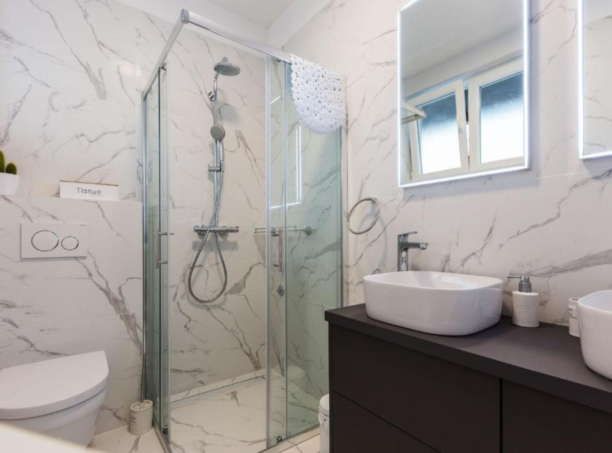 A modern bathroom with a glass-enclosed shower, a white sink, and a dark vanity.