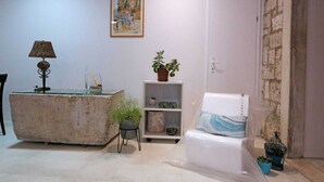 A room with a stone coffee table, a glass-top desk, a potted plant, a bookshelf, a cushioned chair, and a framed artwork on the wall. - Quiet Studio in Zadars Old Town (Zadar)