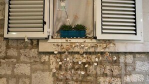 A room with a stone wall, a window with shutters, a small shelf with decorative shells, and a potted plant. - Quiet Studio in Zadars Old Town (Zadar)