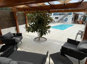 Un patio cubierto con piscina, mobiliario de mimbre y un árbol.