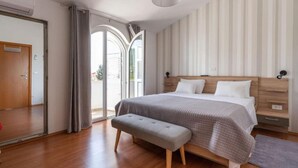 Un dormitorio con una cama grande, un banco, un armario y un ventanal corredera que da a un balcón.