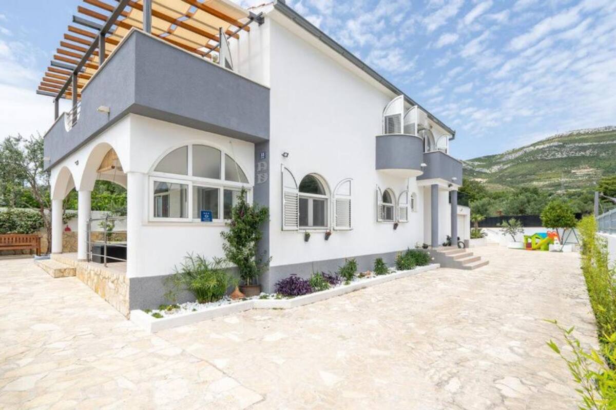 Een modern huis met twee verdiepingen, een stenen terras, witte muren en grijze accenten.