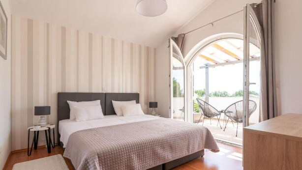 Un dormitorio con una cama grande, una mesita de noche con lámpara, una ventana con cortinas y vistas al exterior.