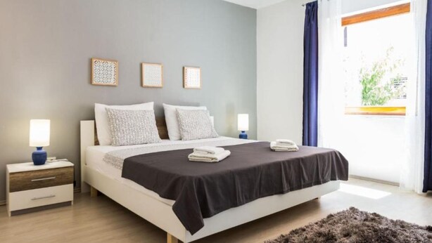 Un dormitorio moderno con una cama grande, mesitas de noche y vistas a zonas verdes a través de la ventana.