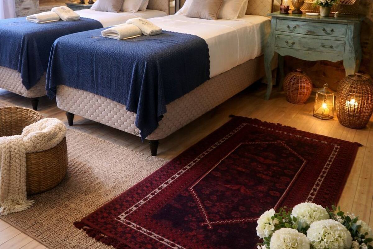 A bedroom with two beds, a chandelier, a stone wall, and a red rug.