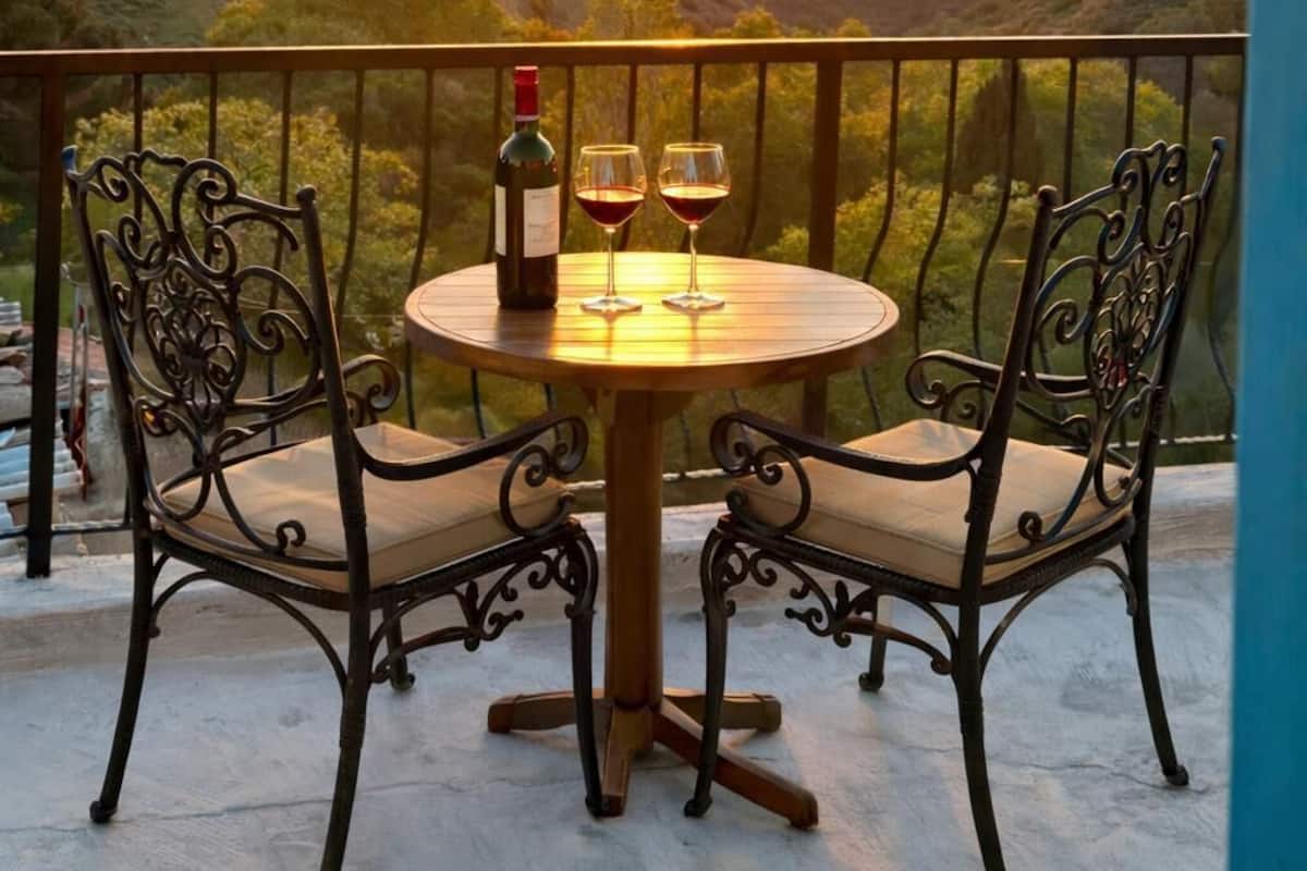 A round table with two chairs on a balcony overlooking a sunset view.