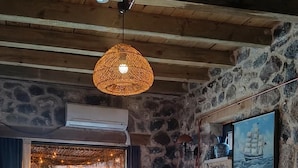 Ein Schlafzimmer mit Steinstruktur, einem Bett mit weißen Leinen, einer Hängelampe und Blick auf einen Sonnenuntergang über dem Wasser.