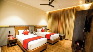 A hotel room with two beds, wooden flooring, a ceiling fan, a TV, and a curtain. - Spree Manor Hotel (Chhatrapati Sambhajinagar)