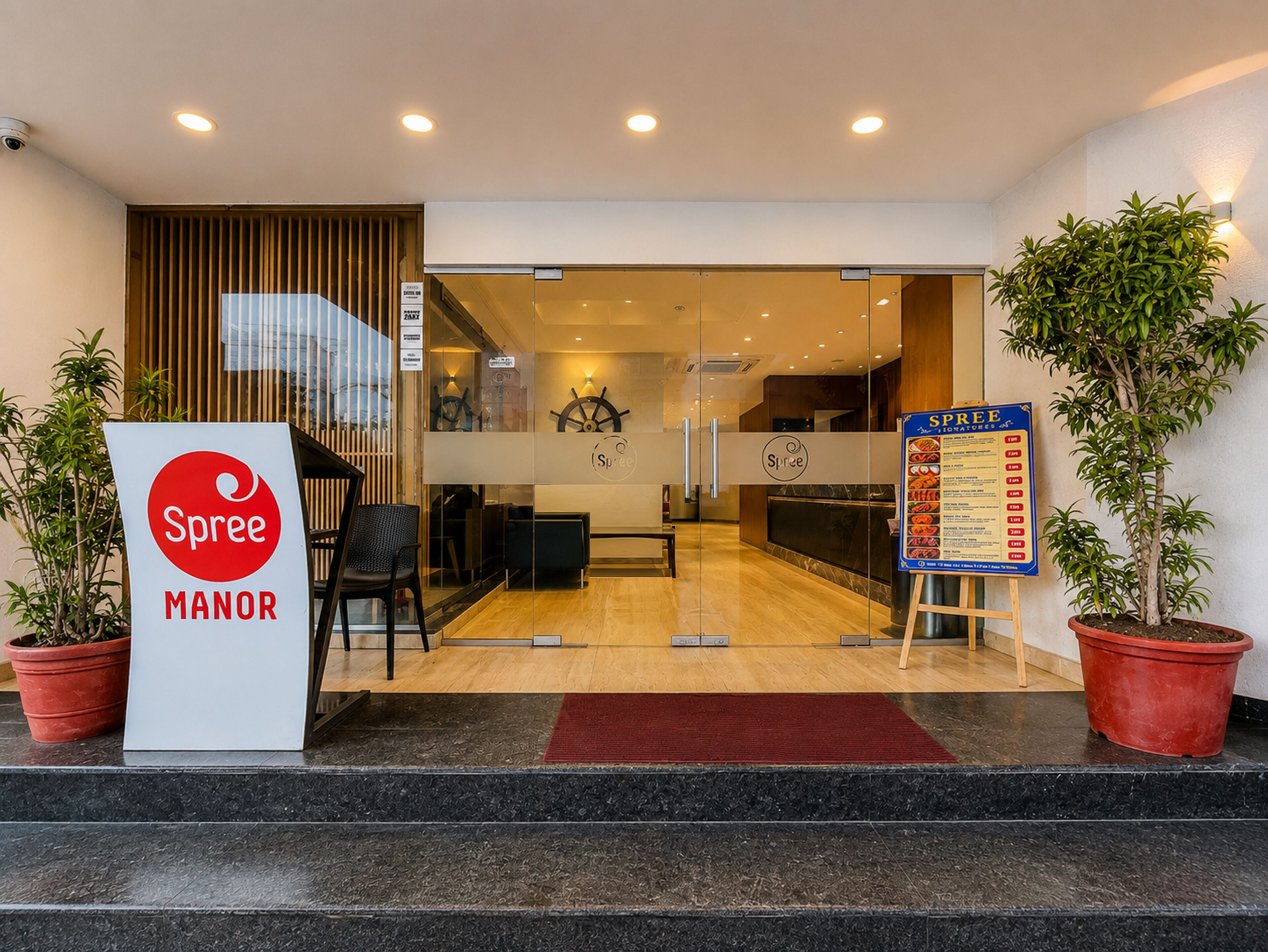 A hotel entrance with a reception desk, a menu board, and potted plants.