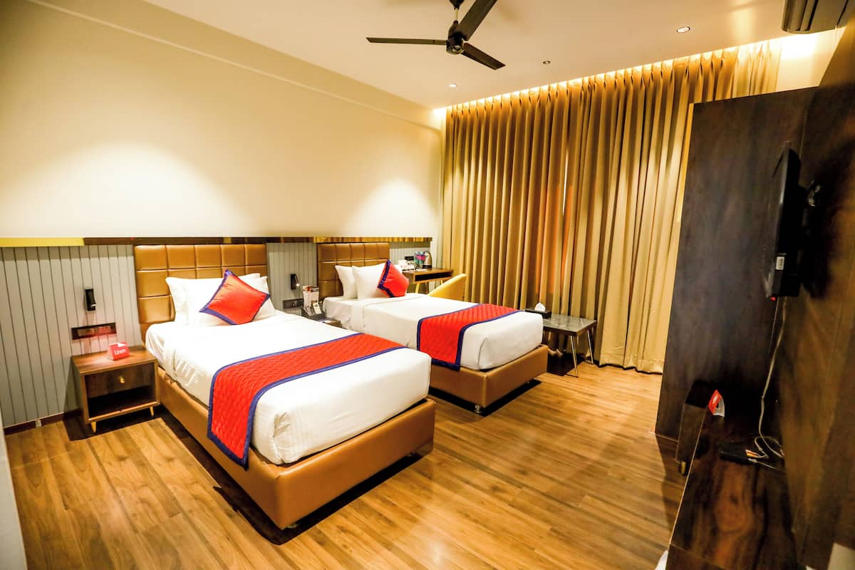 A hotel room with two beds, wooden flooring, a ceiling fan, a TV, and a curtain.
