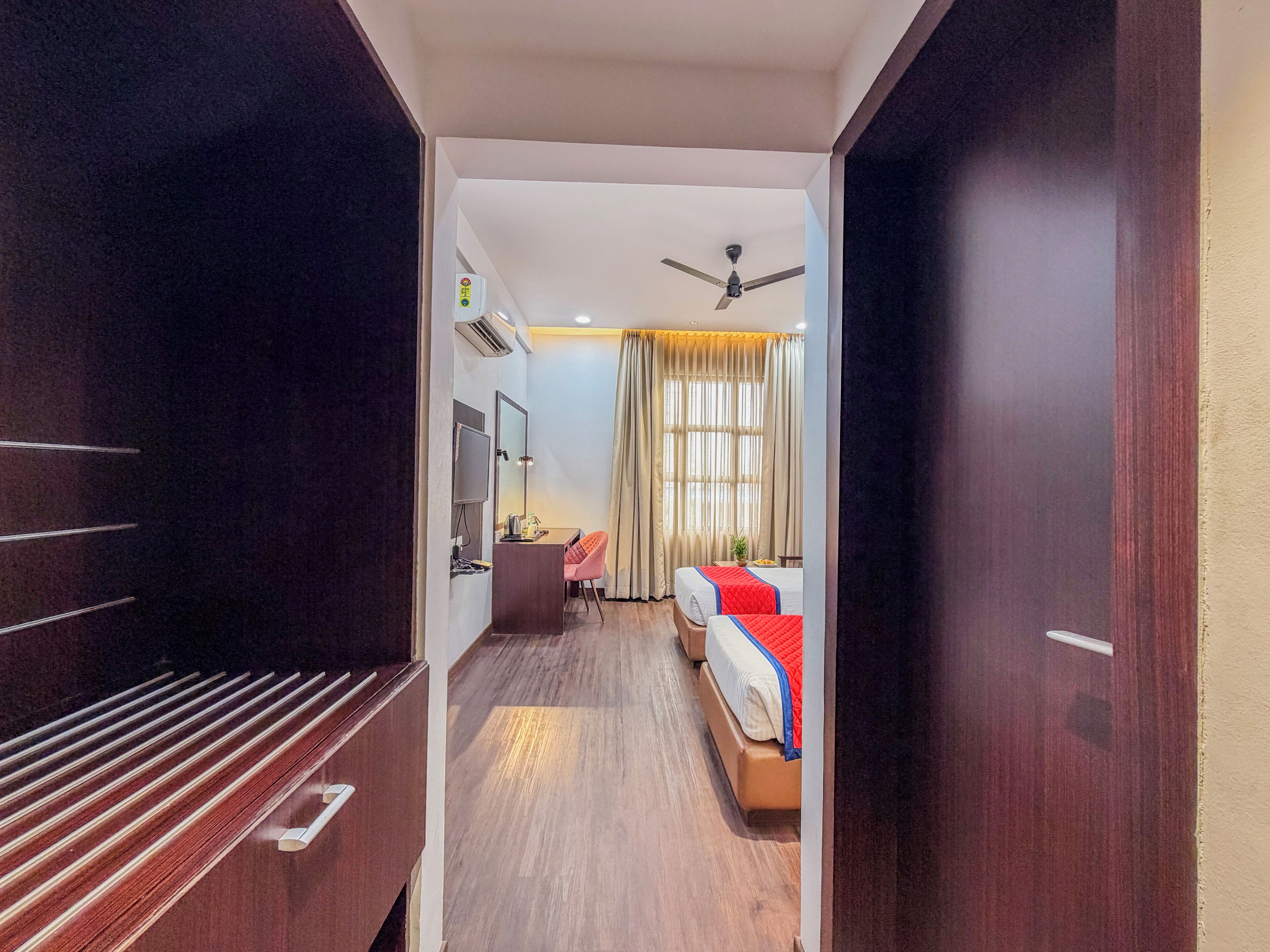 Una habitación de hotel con cama, escritorio, silla, televisión y ventilador de techo.